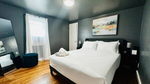 A modern hotel room with a large bed, a bedside table, a chair, and a painting on the wall.