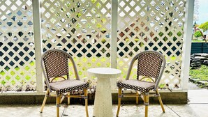 Two wicker chairs with checkered cushions and a round table in front of a lattice fence.