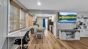 Cozinha moderna com armários brancos, mesa de jantar com cadeiras e uma televisão de tela plana grande na parede.