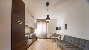 Eine moderne Küche mit Holzausstattung, eine Essecke mit grauem Sofa und einem an der Wand montierten Fernseher.