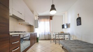 Eine kompakte Küche mit modernen Geräten, ein Essbereich mit Tisch und Stühlen und ein Sofa im Wohnbereich.
