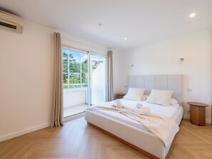 A modern bedroom with a large bed, a sliding glass door to a balcony, and a ceiling-mounted air conditioning unit. - 2-Br Sea-View Apartment – East Cannes (Cannes)
