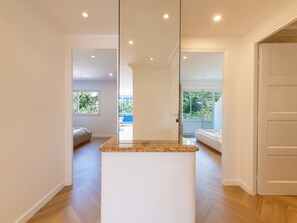 A modern interior with a kitchen island, wooden flooring, and a view of a balcony with greenery. - 2-Br Sea-View Apartment – East Cannes (Cannes)