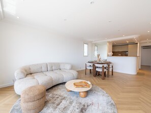 A modern living room with a sectional sofa, a round coffee table, and a dining area with a glass-top table. - 2-Br Sea-View Apartment – East Cannes (Cannes)