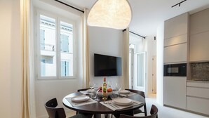 Un espace repas moderne avec une table ronde pour quatre personnes, un téléviseur à écran plat fixé au mur et un coin cuisine équipé d’un four à micro-ondes.