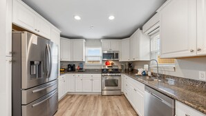 A modern kitchen with white cabinets, stainless steel appliances, and a granite countertop. - Sunflower Yellow Coastal Escape (Galveston)