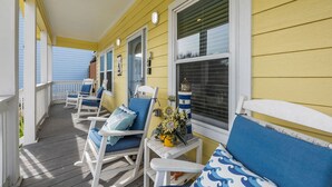 A covered porch with white rocking chairs and blue cushions, yellow siding, and a small table with a vase of sunflowers. - Sunflower Yellow Coastal Escape (Galveston)