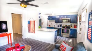 Een compacte keuken met donkerblauwe kastjes, een centraal eiland en een plafondventilator.