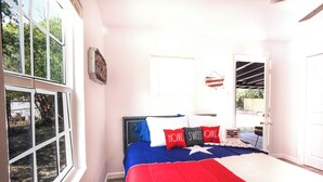 Een slaapkamer met een groot raam, een bed met een deken in rood, wit en blauw, en een deur naar een terras.