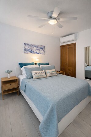 A bedroom with a bed, a nightstand, a ceiling fan, a wall-mounted air conditioner, and a wooden wardrobe. - Poolview Suite in Dominicus Bayahibe (Dominicus)