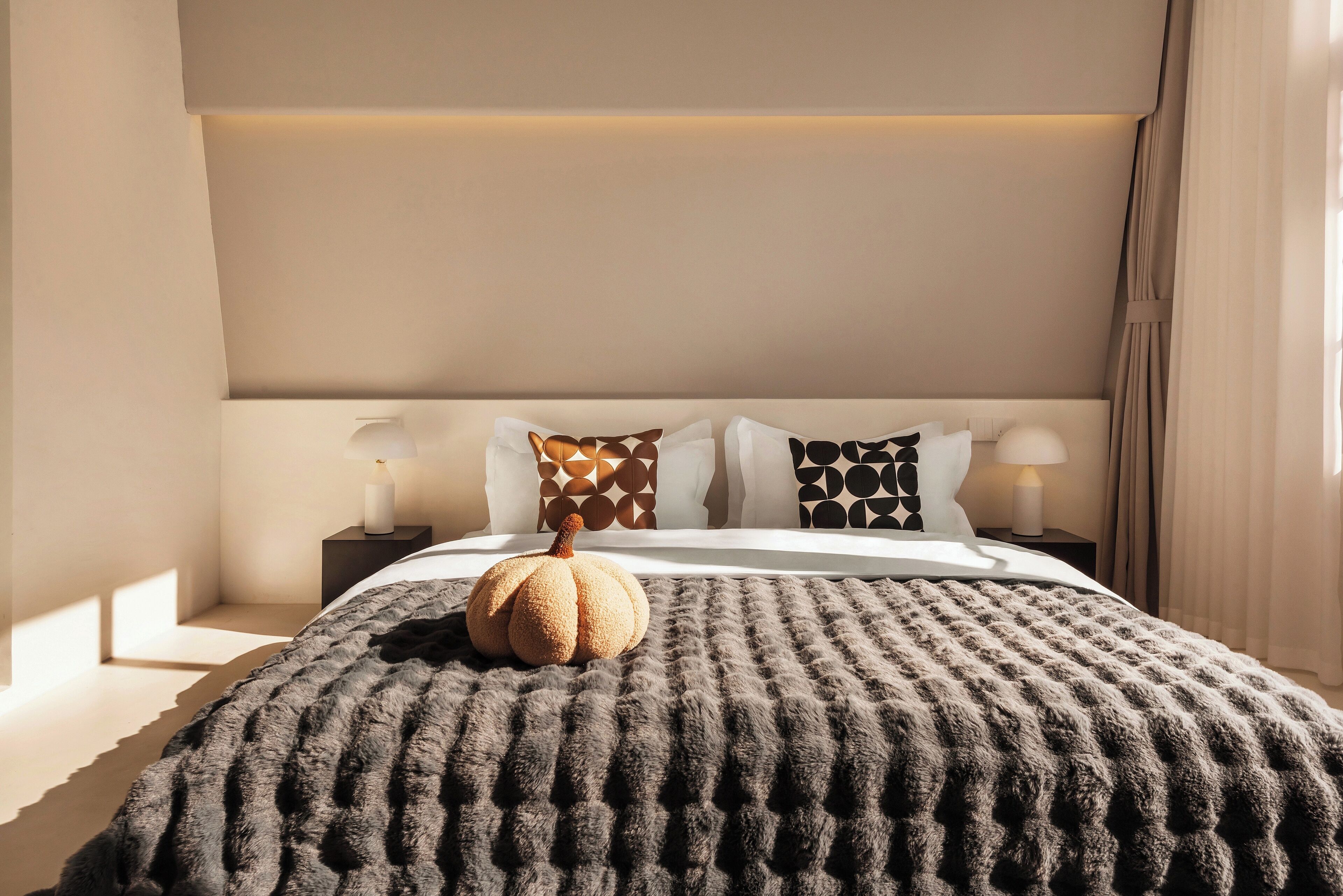 A neatly made bed with a textured blanket, a decorative pumpkin, and patterned pillows.