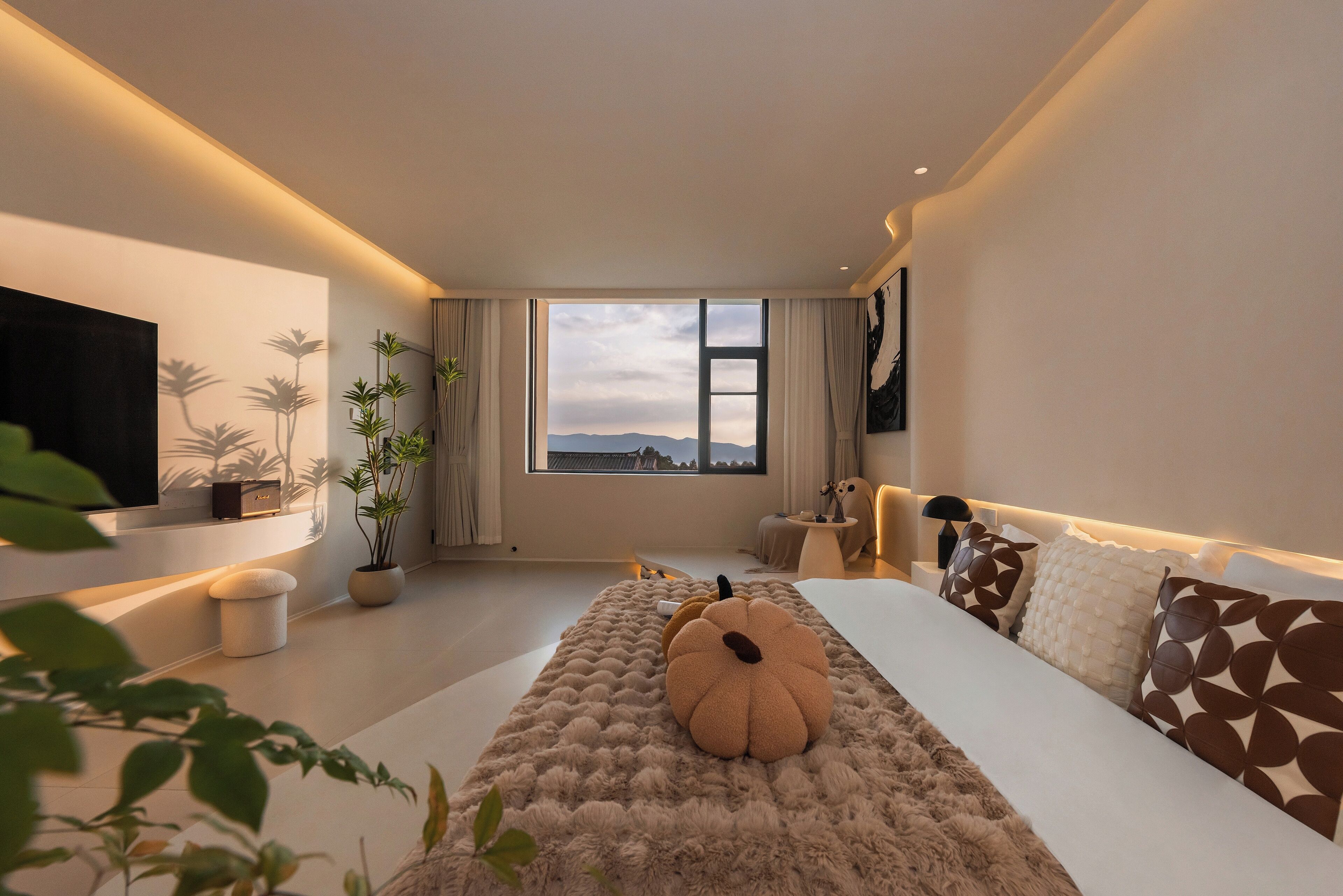 Une chambre moderne avec une grande fenêtre, un téléviseur à écran plat fixé au mur, un lit confortable agrémenté de coussins décoratifs et une table de chevet avec une lampe.