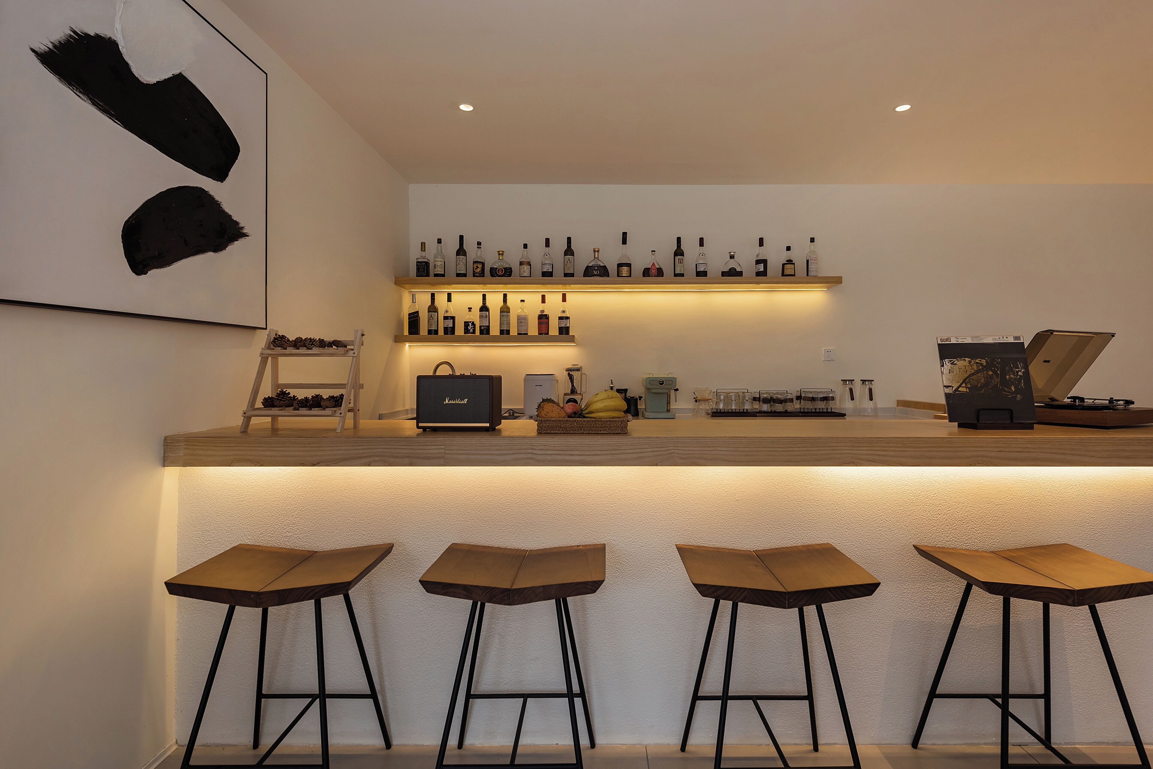 A bar area with a long counter, multiple stools, and a shelf with bottles.