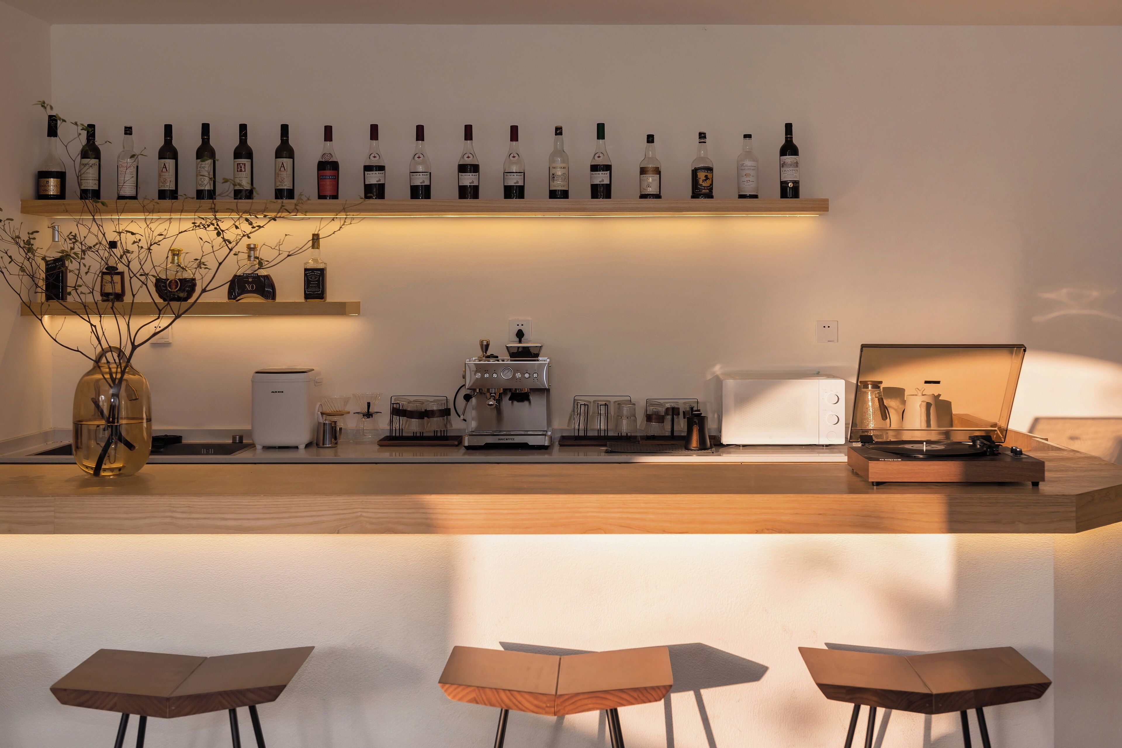 A bar area with multiple wine bottles on shelves, a coffee machine, and a turntable.
