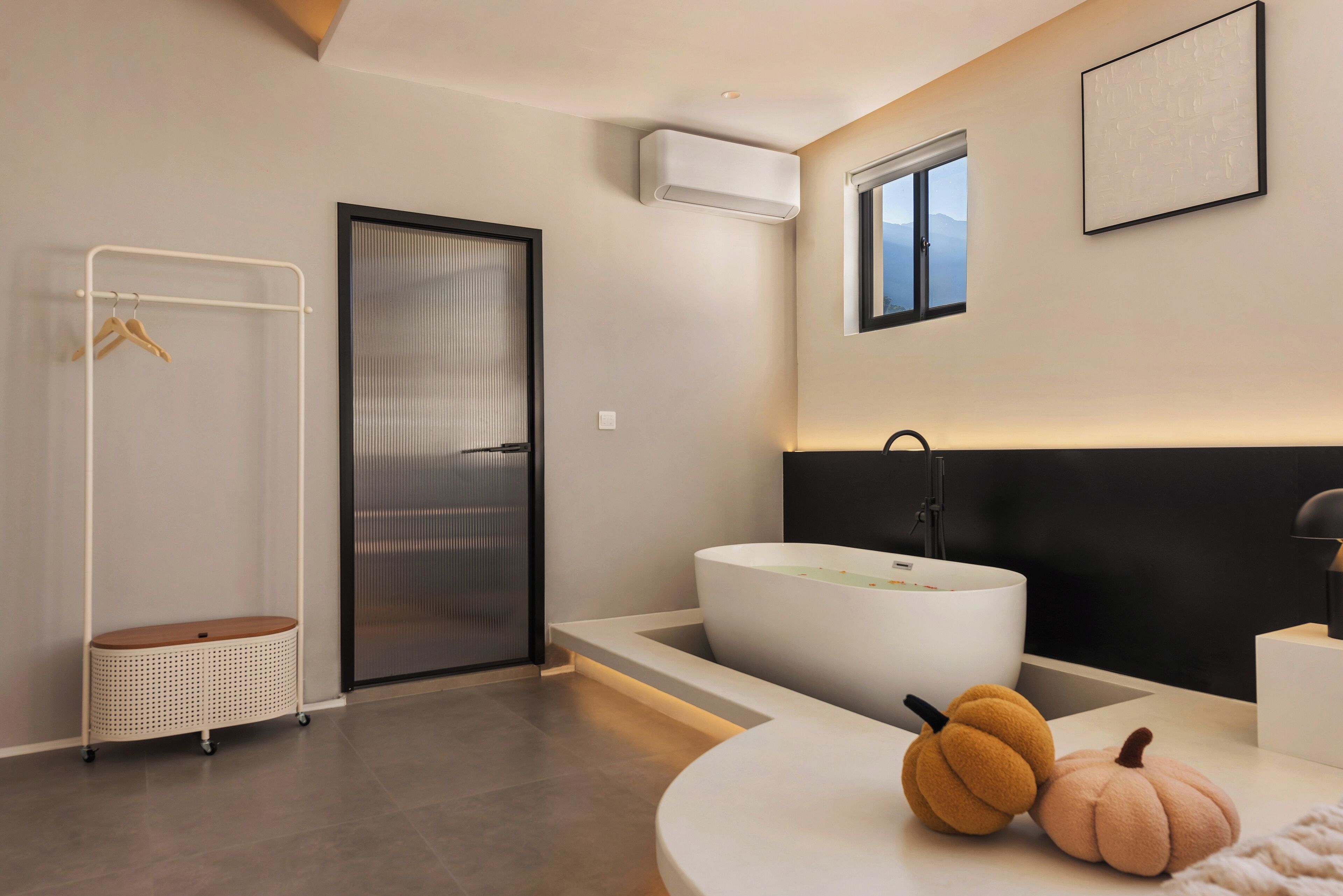 A modern bathroom with a freestanding bathtub, a towel rack, and a small table with decorative pumpkins.