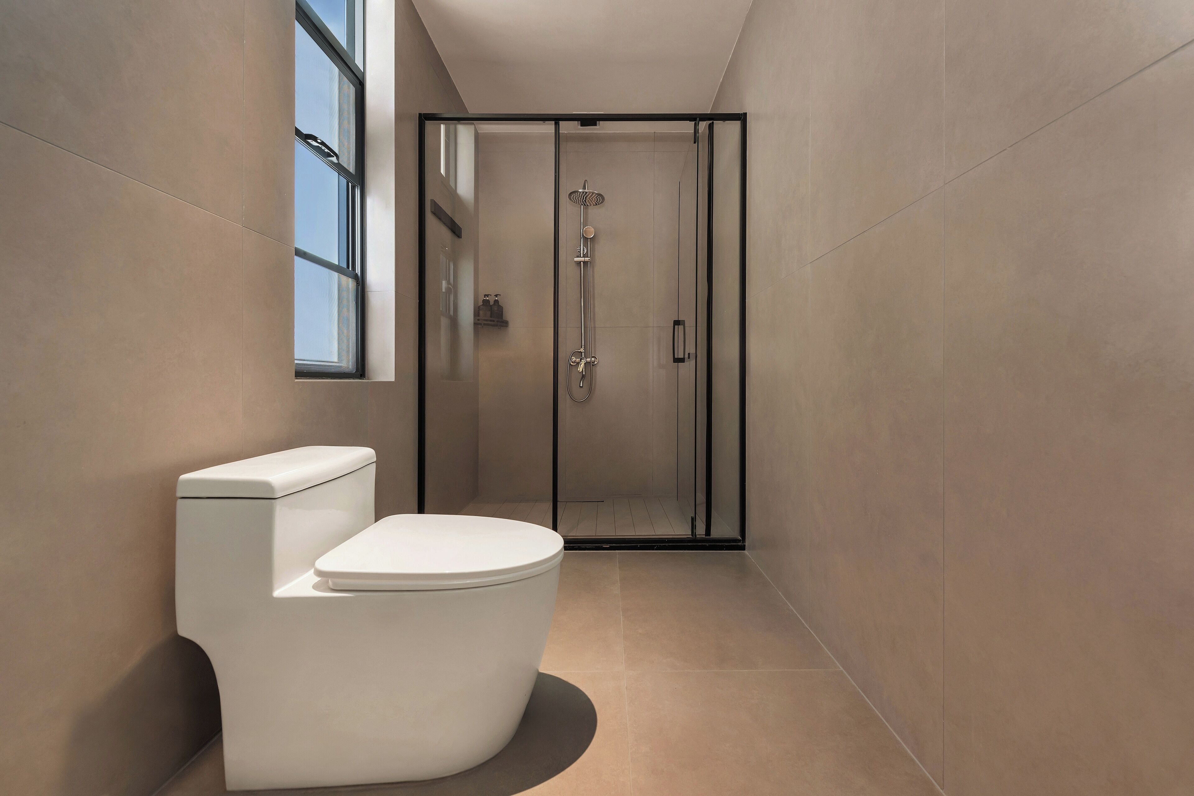 Un baño moderno con inodoro, ducha con mampara de vidrio y ventana que proporciona luz natural.