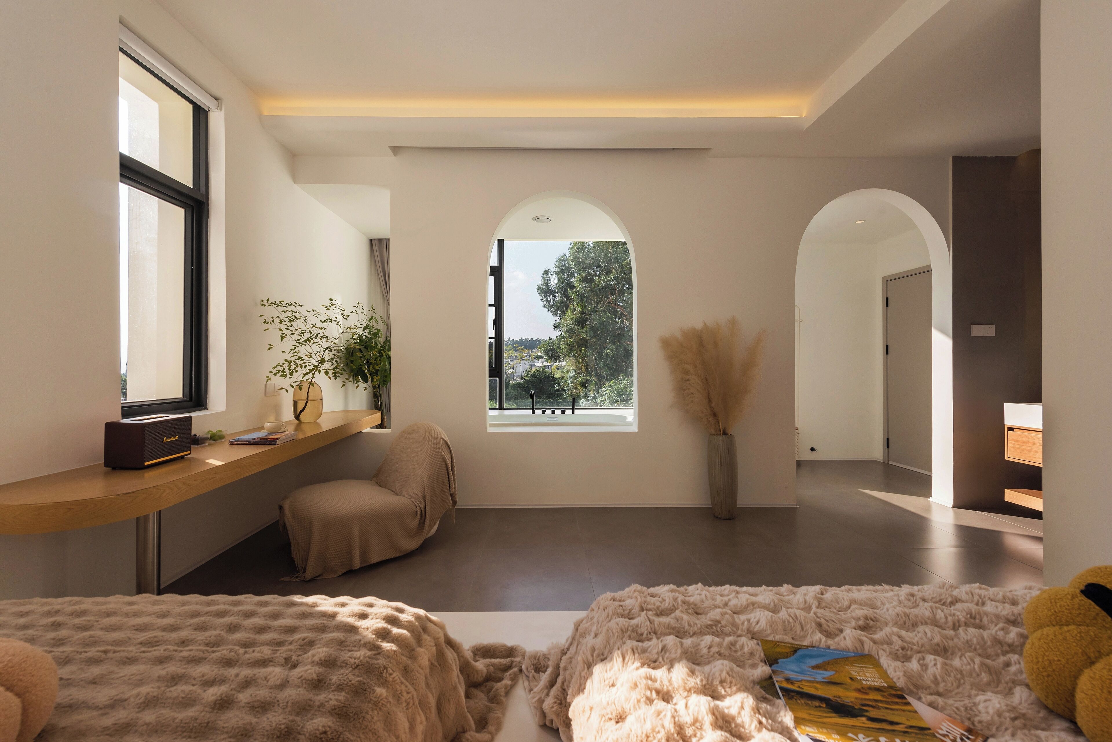 A modern bedroom with a large window, a sofa, a fluffy rug, and a bedside table with a lamp.