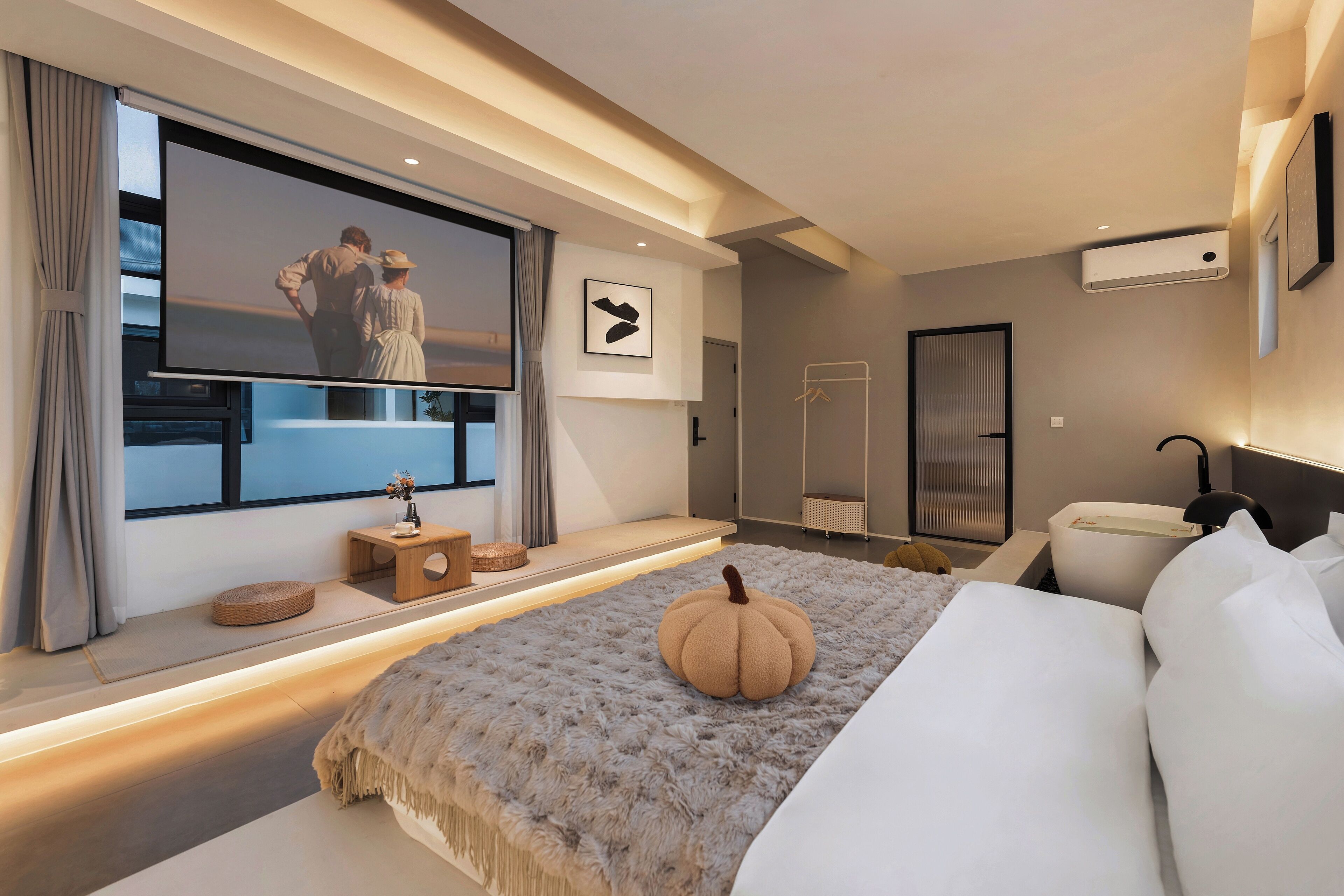 A modern hotel room with a large bed, a television, a window with curtains, a small side table, and a wall-mounted air conditioning unit.