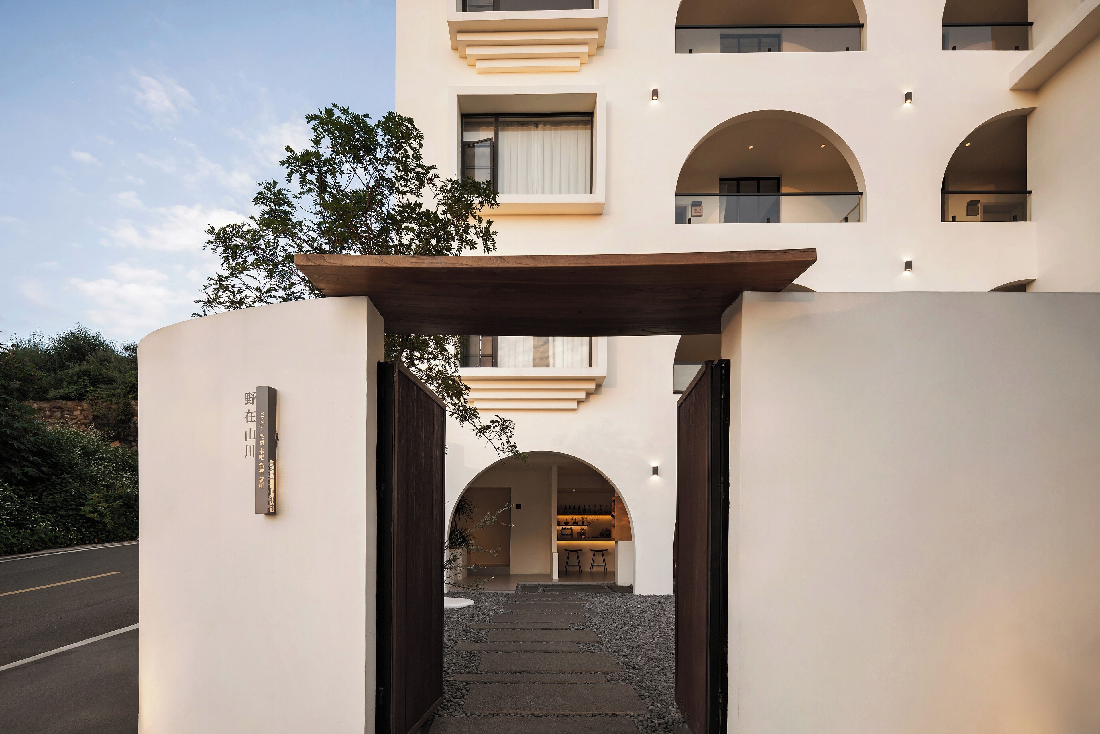 Uma entrada de hotel moderna com uma cobertura que leva ao saguão, apresentando um design minimalista e vista para a paisagem circundante.