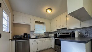 A compact kitchen with white cabinets, a stainless steel refrigerator, a microwave, a stove, and a coffee maker. - Duke Stayhouse (Durham)