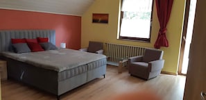Une chambre à coucher avec un lit, deux chaises, un radiateur et une fenêtre avec des rideaux.