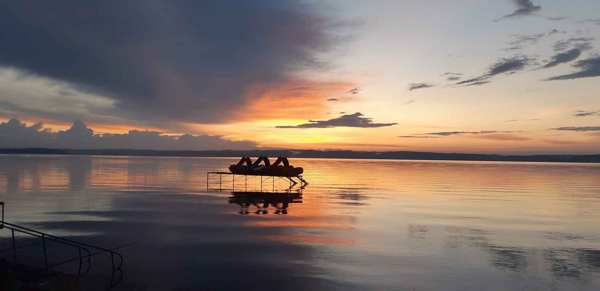 A calm lake at sunset with a boat carrying people.