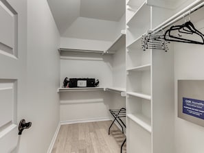 A walk-in closet with white walls, a wooden floor, and a hanging rod with clothes.