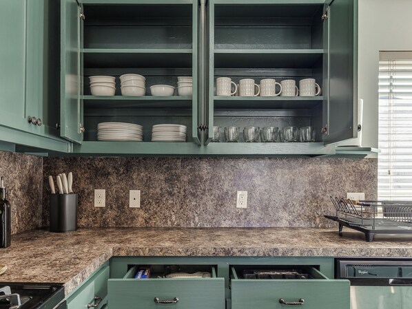 A kitchen with green cabinets, granite countertops, and a built-in dishwasher.