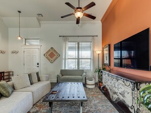 A living room with a sofa, a coffee table, a TV, a ceiling fan, and a window with curtains.