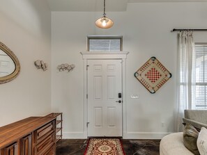 A hallway with a white door, a wooden console table, a patterned rug, a wall-mounted chessboard, and a hanging light fixture. - Antique and Modern Charming 3-bedroom home, 7 mins to Paycom & Convention Center (Oklahoma City)