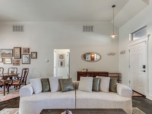 A living room with a sectional sofa, a dining area with a wooden table and chairs, and a hallway with a door and a mirror.