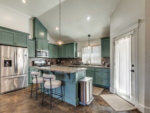 A kitchen with teal cabinets, stainless steel appliances, and a central island with bar stools.