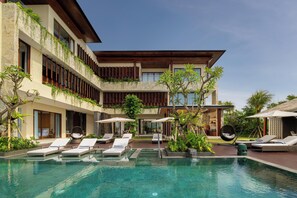 Un hotel moderno con piscina, sillones de descanso y un jardín bien cuidado.