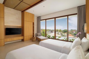 Habitación de hotel moderna con televisor grande, dos camas, zona de estar y vista a la ciudad.