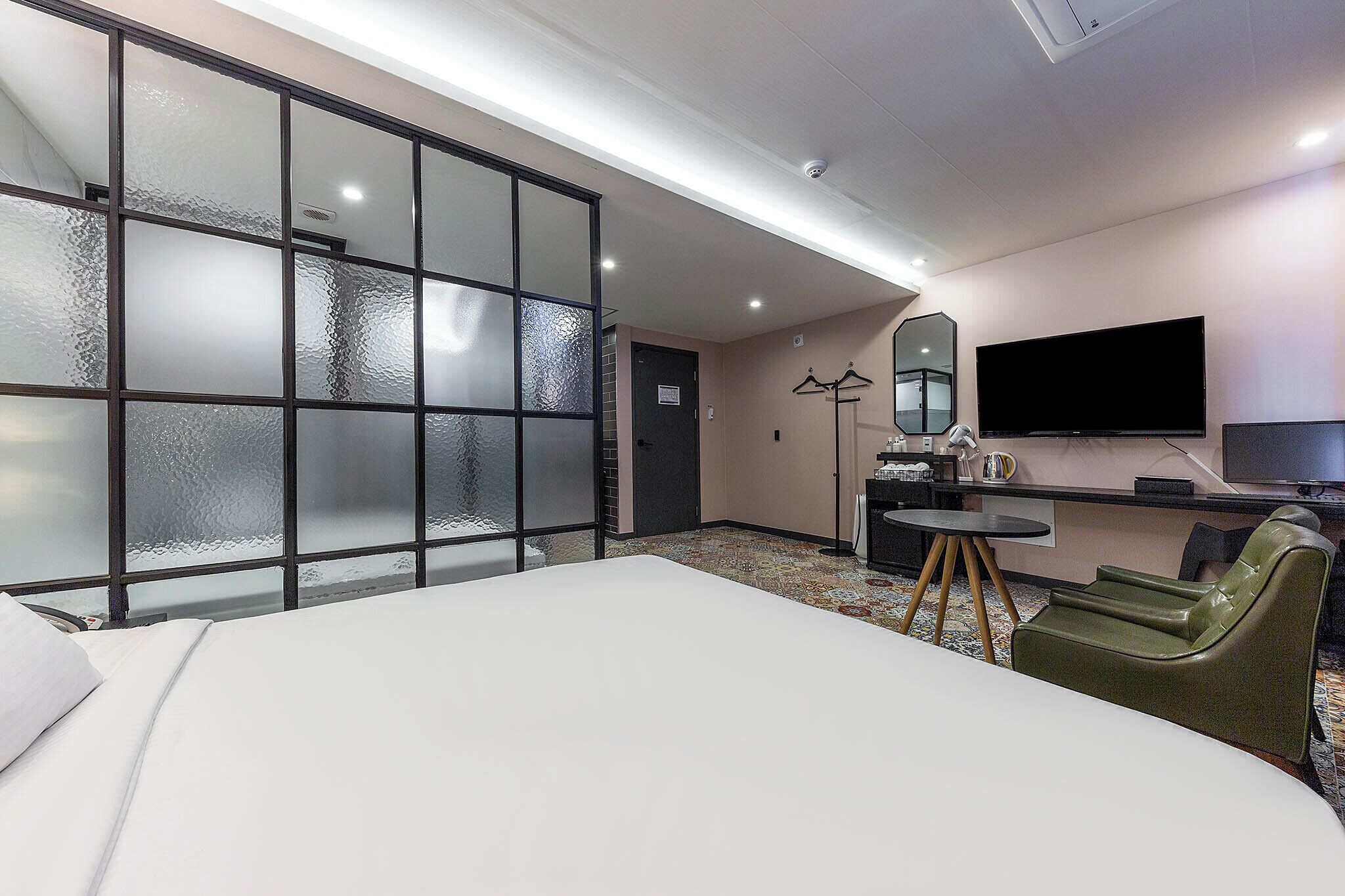 A hotel room with a large bed, a desk with a chair, a television, and a sliding door with frosted glass panels.