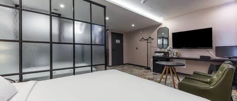 A hotel room with a large bed, a desk with a chair, a television, and a sliding door with frosted glass panels.