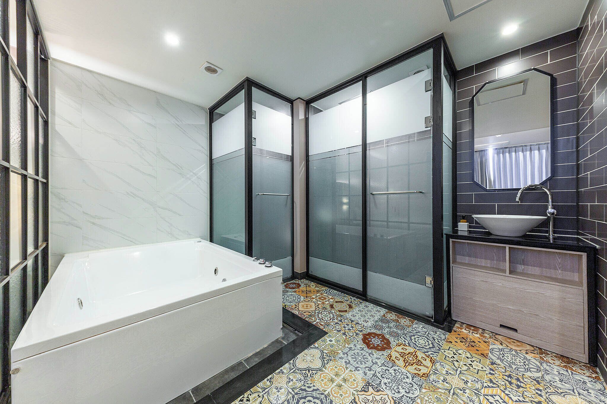 A modern bathroom with a large bathtub, frosted glass shower doors, a sink with a vessel basin, and a patterned floor.