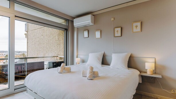 Ein modernes Hotelzimmer mit einem großen Bett, einem Balkon mit Blick und einer wandmontierten Klimaanlage.