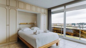Ein modernes Schlafzimmer mit großem Bett, Einbauschränken und Blick auf die Stadt durch ein großes Fenster.