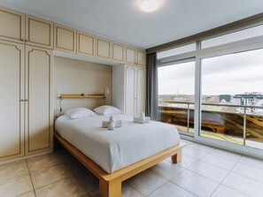 Ein modernes Schlafzimmer mit großem Bett, Einbauschränken und Blick auf die Stadt durch ein großes Fenster.