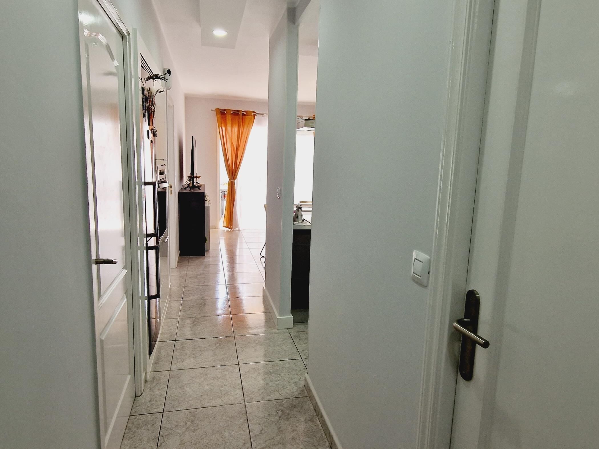 Un pasillo con piso de baldosas que conduce a una habitación con ventana y cortinas.