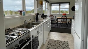 A modern kitchen with a gas stove, sink, and white cabinets. There is a dining area with a table and chairs.
