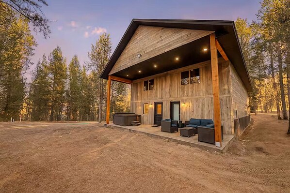 A rustic cabin with a covered porch, large windows, and a fire pit area.