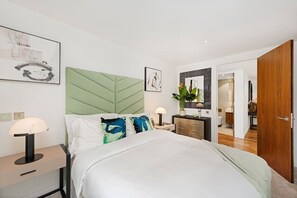 A modern bedroom with a large bed, a green upholstered headboard, bedside tables with lamps, and artwork on the walls. - Exclusive Fitzrovia 3-bed Concierge Central AC (London)