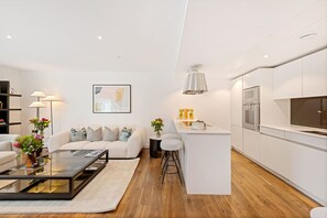 A modern living room with a sofa, coffee table, and a small kitchen area with a bar counter. - Exclusive Fitzrovia 3-bed Concierge Central AC (London)