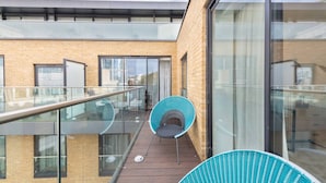 Un edificio moderno con balcón de vidrio, terraza de madera y una silla azul.