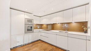 Una cocina moderna con armarios blancos, un horno de acero inoxidable, piso de madera y una pequeña planta en la encimera.