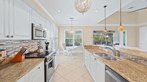 A kitchen with white cabinets, a granite countertop, stainless steel appliances, and pendant lighting. - Bonita Breeze | Prime Location | Screened Pool & Spa (Bonita Springs)