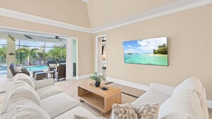 A living room with a pool view, beige walls, and a mounted TV. - Bonita Breeze | Prime Location | Screened Pool & Spa (Bonita Springs)