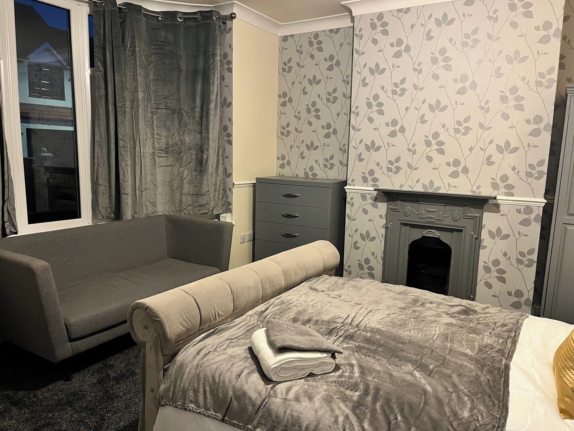 A bedroom with a bed, a sofa, a dresser, and a fireplace.